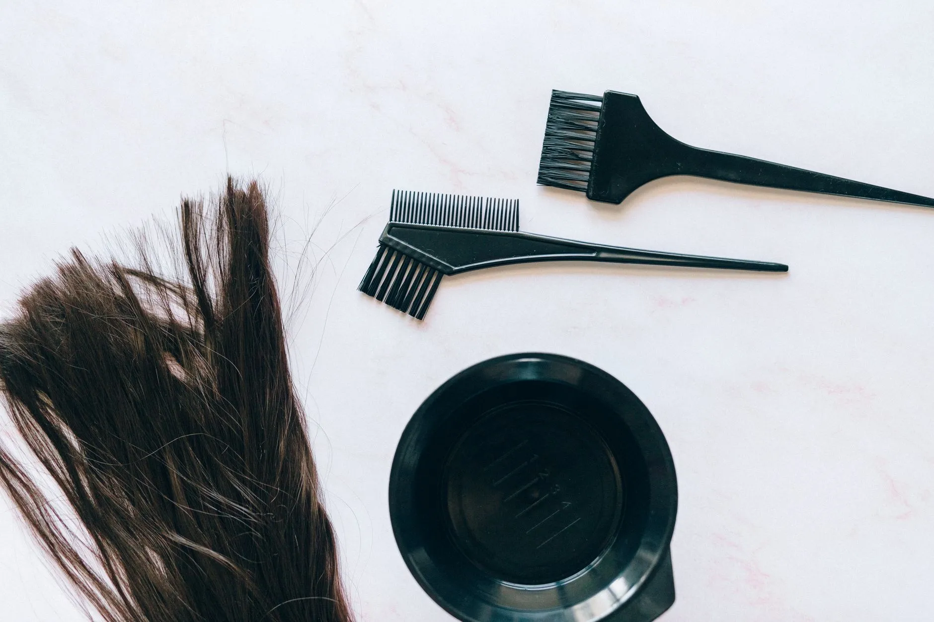 Tint bowl, colour brush and strands of hair on a white surface